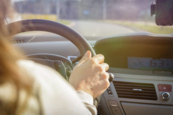 Woman driving a car, close up of her hand at the steering  wheel. View from behind